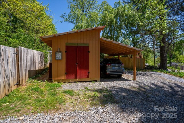 view of shed featuring fence, driveway, and a carport