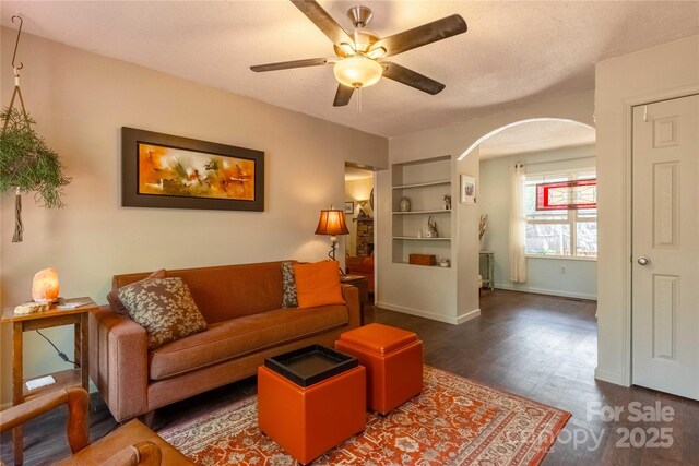 living area with baseboards, arched walkways, ceiling fan, and wood finished floors