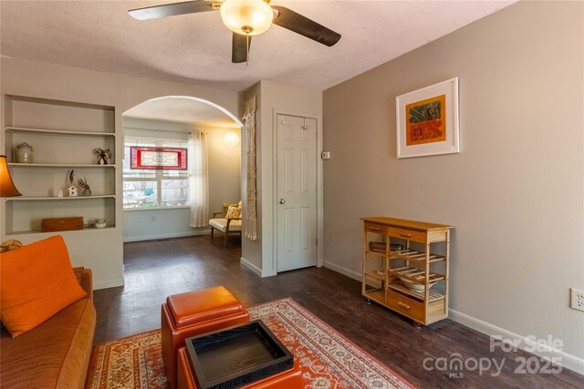 sitting room with baseboards, arched walkways, a ceiling fan, and wood finished floors