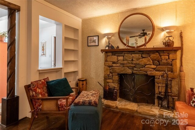 sitting room featuring wood finished floors, a fireplace, ceiling fan, a textured ceiling, and built in shelves