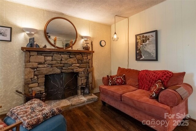living room featuring a stone fireplace, a textured ceiling, and wood finished floors
