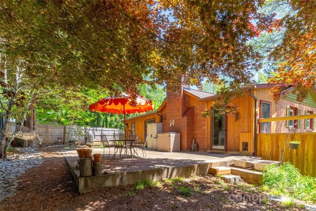 rear view of property featuring a chimney, a deck, brick siding, a fenced backyard, and outdoor dining space