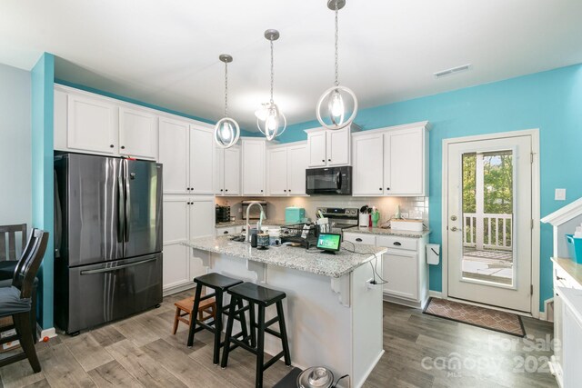 kitchen with a sink, a kitchen breakfast bar, stainless steel appliances, white cabinetry, and wood finished floors