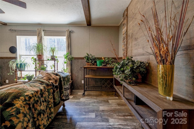 sitting room with a ceiling fan, a textured ceiling, wood finished floors, and beamed ceiling