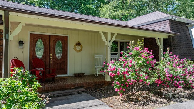 view of exterior entry with covered porch and roof with shingles