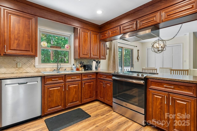 kitchen featuring light stone counters, a sink, light wood-style floors, stainless steel appliances, and under cabinet range hood