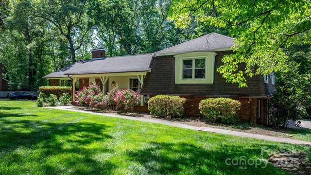 split level home with a chimney, brick siding, roof with shingles, and a front yard