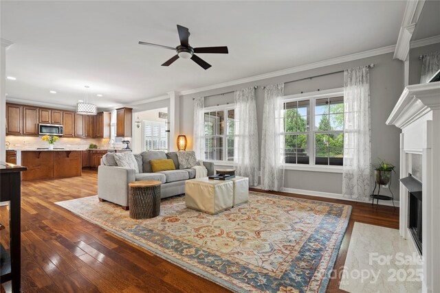 living area with a fireplace, ceiling fan, ornamental molding, light wood-type flooring, and recessed lighting