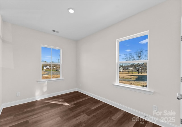 spare room featuring dark wood-style flooring, baseboards, visible vents, and plenty of natural light