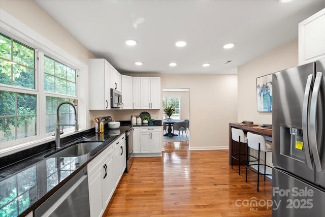 kitchen featuring stainless steel appliances, white cabinetry, a sink, and light wood-type flooring