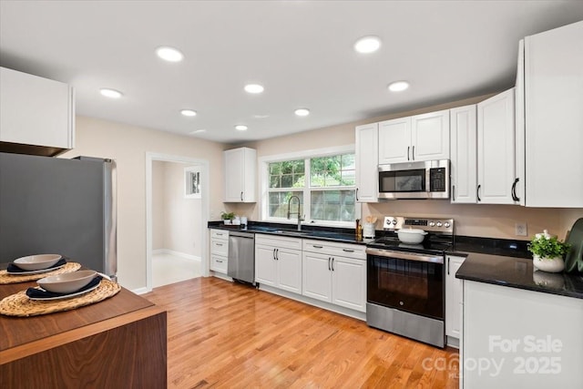 kitchen with dark countertops, light wood-style floors, white cabinetry, a sink, and stainless steel appliances