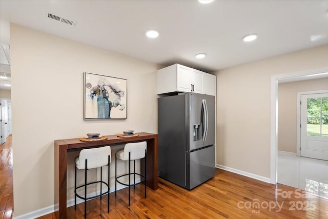 kitchen with visible vents, wood finished floors, baseboards, white cabinets, and stainless steel fridge with ice dispenser