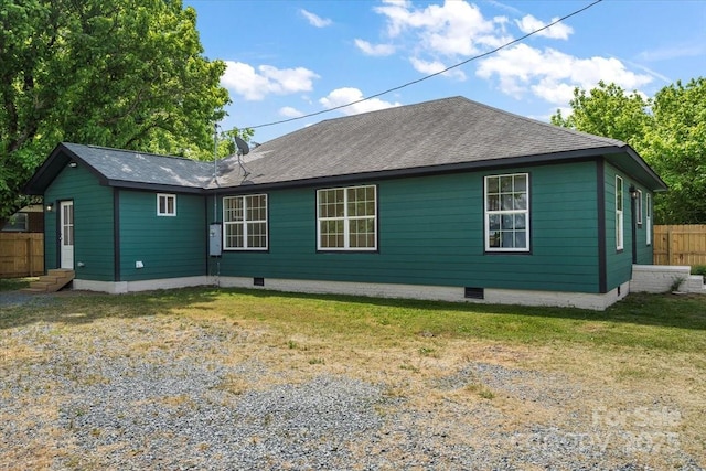 rear view of house with fence, a shingled roof, a yard, and crawl space