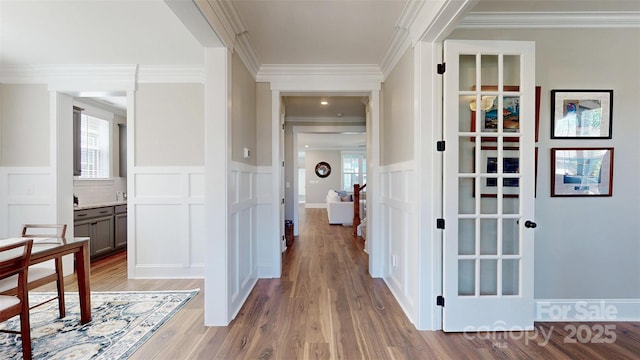 hall with ornamental molding, a decorative wall, a healthy amount of sunlight, and a wainscoted wall
