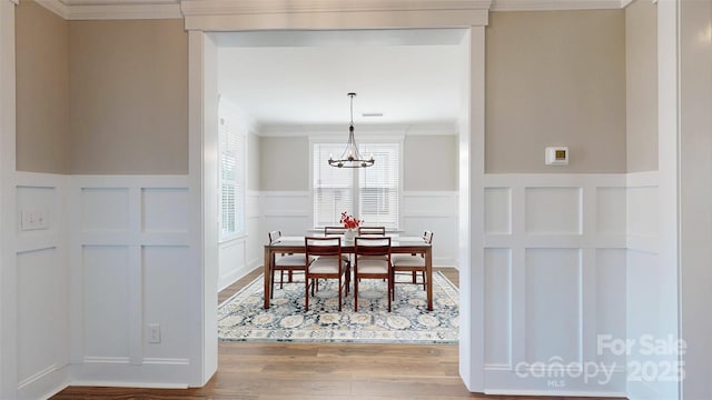 dining area featuring wainscoting, wood finished floors, a chandelier, ornamental molding, and a decorative wall