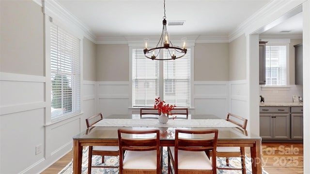 dining space with a chandelier, a healthy amount of sunlight, light wood finished floors, and a decorative wall