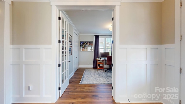 corridor featuring a decorative wall, ornamental molding, wood finished floors, and a wainscoted wall