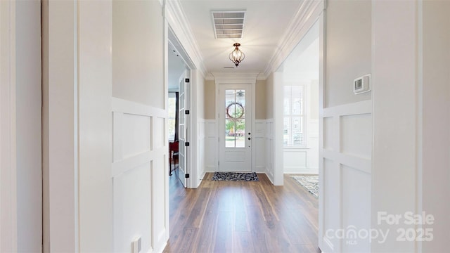 entryway featuring visible vents, crown molding, a decorative wall, wood finished floors, and a wainscoted wall