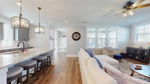 living room featuring crown molding, baseboards, ceiling fan with notable chandelier, and dark wood-style floors