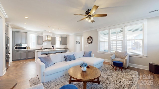 living area featuring visible vents, light wood-style flooring, baseboards, and a wealth of natural light