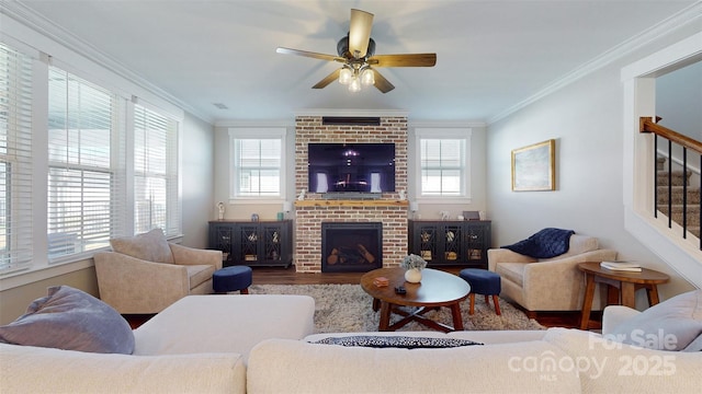 living area with ornamental molding, a brick fireplace, wood finished floors, ceiling fan, and stairway
