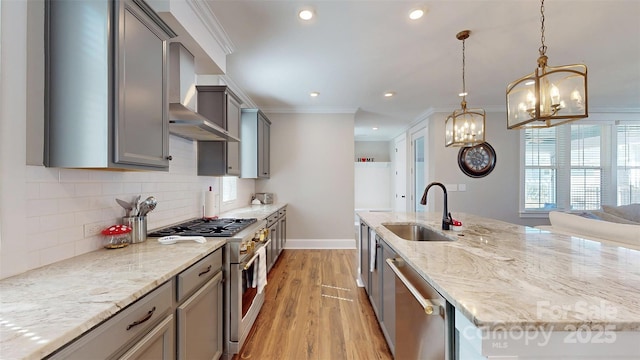 kitchen featuring wall chimney range hood, a sink, light wood finished floors, appliances with stainless steel finishes, and gray cabinetry