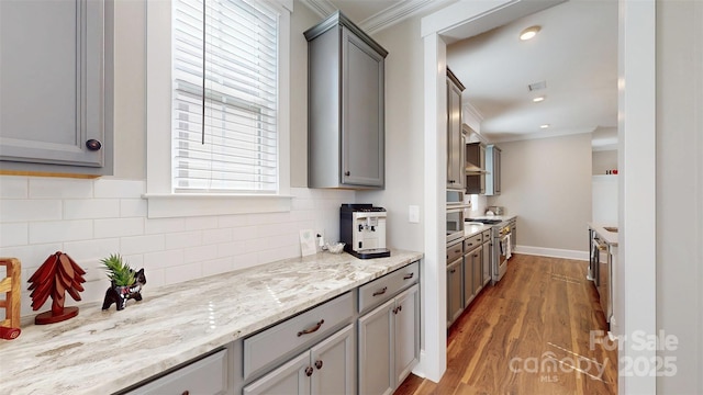 kitchen featuring stainless steel appliances, decorative backsplash, wood finished floors, gray cabinetry, and ornamental molding