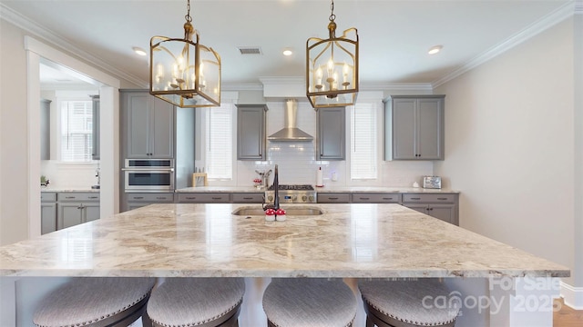 kitchen featuring decorative backsplash, gray cabinets, wall chimney exhaust hood, and a notable chandelier