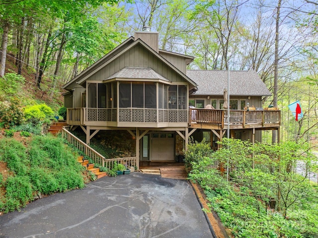 chalet / cabin with a chimney, roof with shingles, a sunroom, a garage, and aphalt driveway