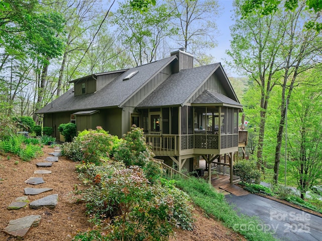 exterior space featuring a shingled roof, a sunroom, and a chimney