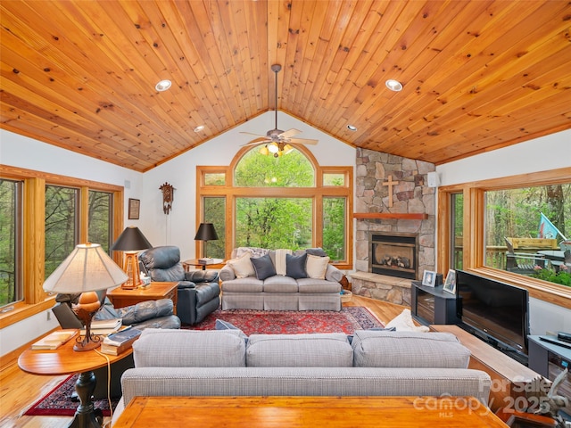 living room with plenty of natural light, a stone fireplace, wood finished floors, and lofted ceiling