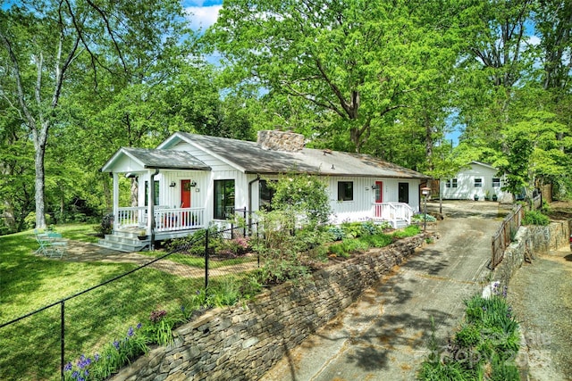 ranch-style home featuring fence, aphalt driveway, board and batten siding, a chimney, and covered porch
