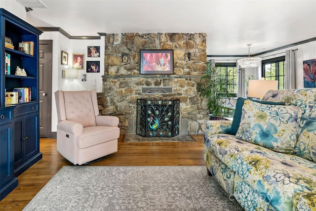 living area with crown molding, wood finished floors, a stone fireplace, and an inviting chandelier