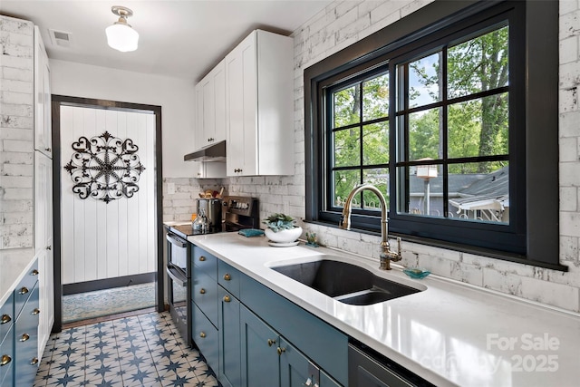 kitchen with light floors, under cabinet range hood, range with two ovens, a sink, and blue cabinetry