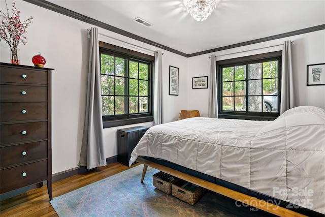 bedroom featuring baseboards, ornamental molding, wood finished floors, and visible vents
