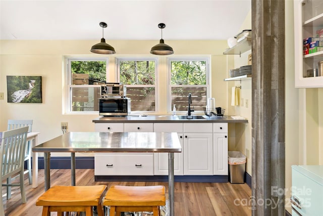 kitchen with light wood finished floors, stainless steel microwave, white cabinets, and a wealth of natural light