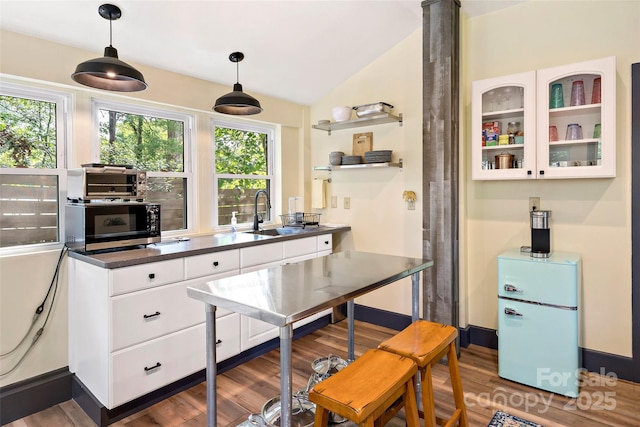 kitchen featuring decorative light fixtures, dark countertops, wood finished floors, a sink, and white cabinets
