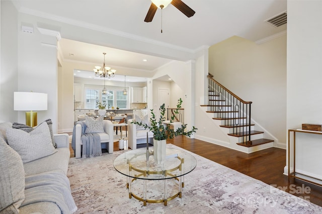 living area with wood finished floors, a chandelier, ornamental molding, stairs, and a ceiling fan
