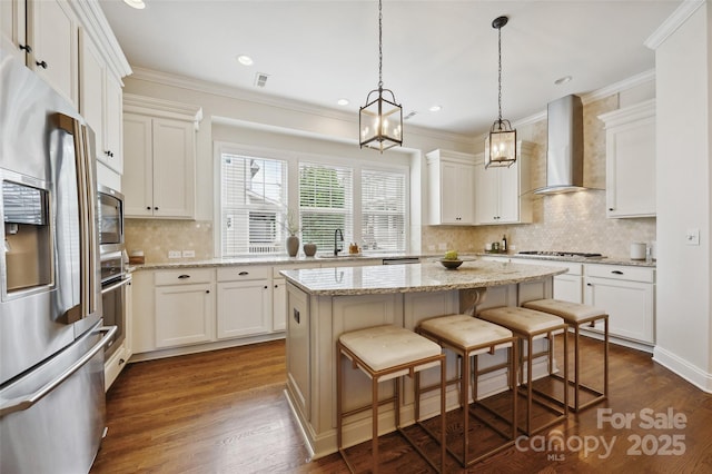 kitchen featuring appliances with stainless steel finishes, wall chimney exhaust hood, a sink, a center island, and decorative backsplash