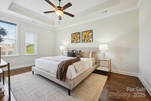 bedroom featuring a raised ceiling, ornamental molding, dark wood-type flooring, baseboards, and ceiling fan