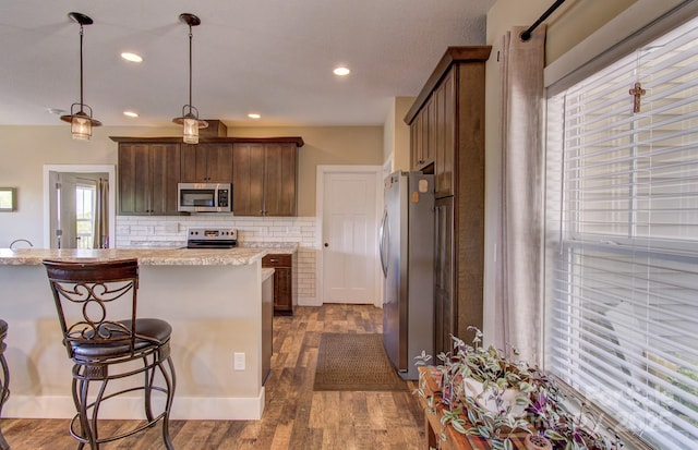 kitchen featuring stainless steel appliances, tasteful backsplash, a kitchen breakfast bar, dark wood-type flooring, and hanging light fixtures
