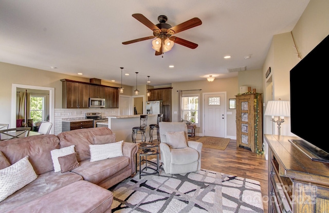 living room featuring light wood-type flooring, a wealth of natural light, ceiling fan, and visible vents