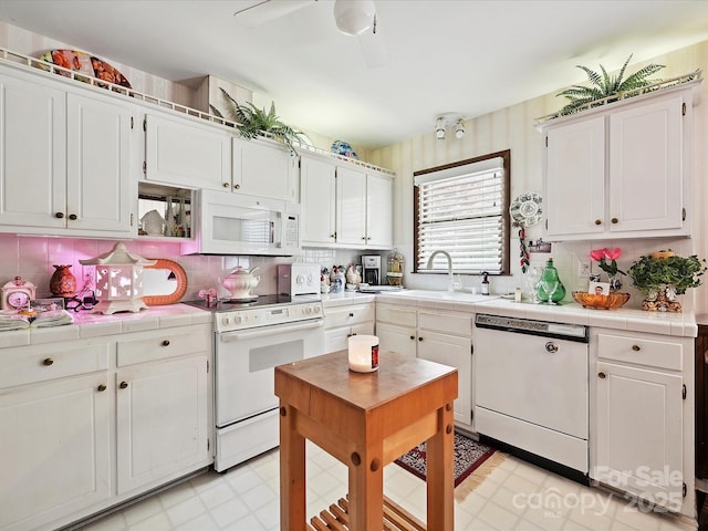 kitchen featuring white cabinetry, tile counters, a sink, and white appliances