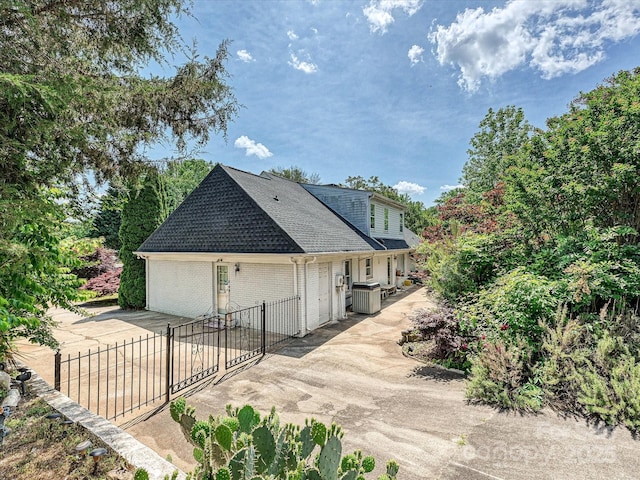 view of property exterior featuring fence, roof with shingles, brick siding, driveway, and a patio area
