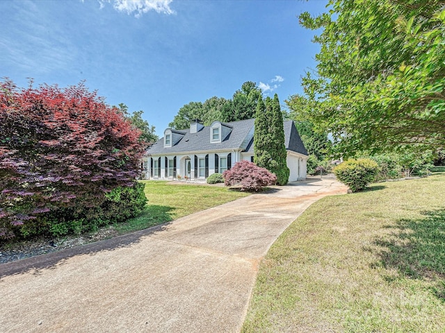 new england style home with a front yard, an attached garage, and driveway
