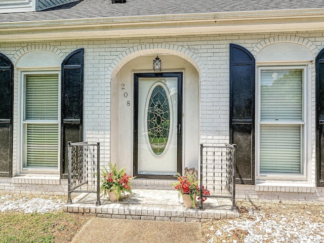 view of exterior entry featuring roof with shingles and brick siding