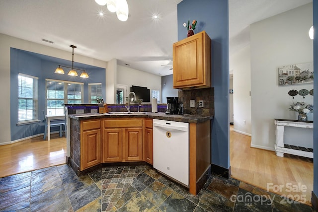 kitchen with white dishwasher, a sink, a peninsula, baseboards, and brown cabinetry