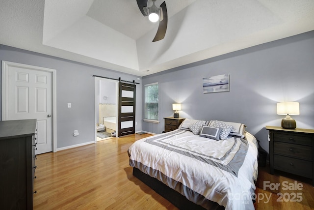 bedroom with light wood-type flooring, a barn door, baseboards, connected bathroom, and a ceiling fan