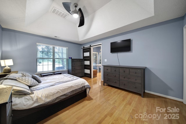bedroom featuring a barn door, light wood-style flooring, ceiling fan, baseboards, and vaulted ceiling