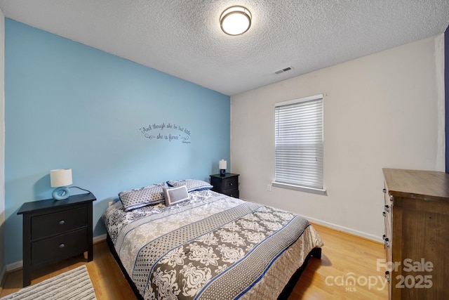 bedroom with wood finished floors, a textured ceiling, and baseboards